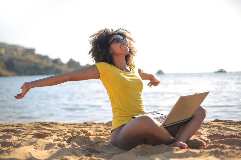 Young woman sitting at the beach, using her laptop to research free backup software