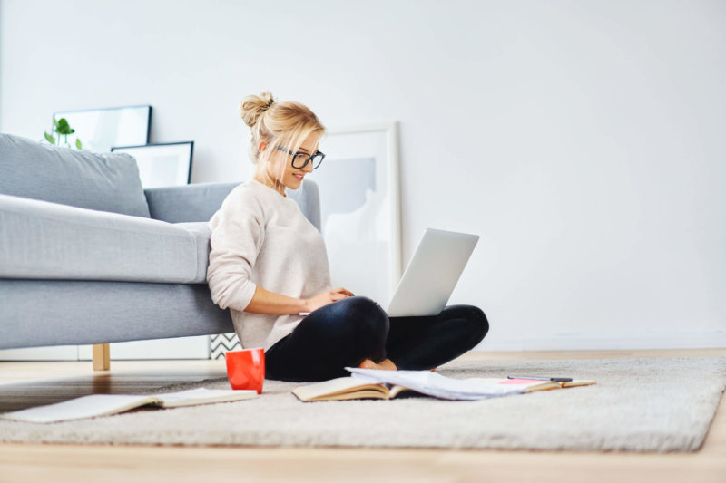 Female student sitting on floor of her apartment with laptop and notes studying. Top free tools for working from home concept.